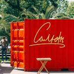 Bright red container with text outdoors amid greenery, sunny day.